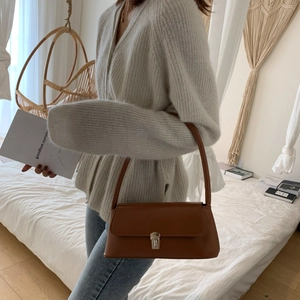 Sac baguette chic en cuir marron avec boucle en métal argenté et bandoulière dans une chambre