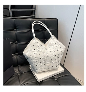 Detail of white tote bag with black bow prints and metal logo plate on a leather chair