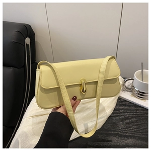 Detail of a creamy yellow leather baguette bag with a gold oval twist lock closure
