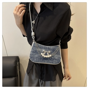 Detail of blue denim crescent bag with silver bow clasp and pearl chain strap