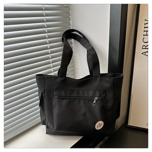 Close-up of black canvas tote bag featuring front zipper pocket and 'good luck!' patch label