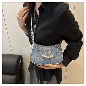 Detail of light blue denim bag with silver butterfly charm and pearl tassel chain