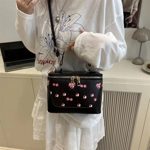 Chic black box handbag with red cherry print and gold zippers shown on a model