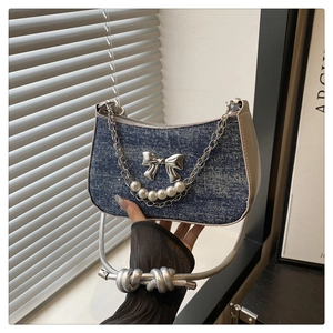 Detail of crescent denim bag featuring silver butterfly charm and pearl chain accent