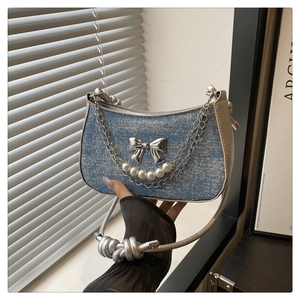Detail of blue denim shoulder bag with silver bow charm and pearl chain decoration