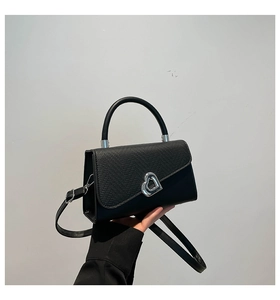 Detail of black crossbody bag featuring grainy leather flap and silver heart rotary clasp