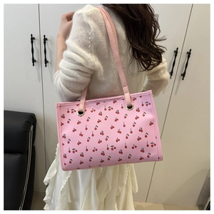 Dettaglio della borsa a spalla rosa con stampa di ciliegie rosse indossata da modella