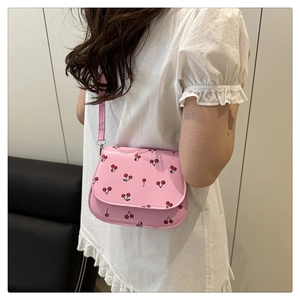 Detail of pink mini crossbody bag with cherry print worn over a white lace dress