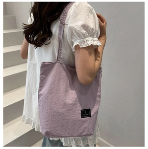 Close-up of lavender fabric tote bag with brand label on light purple pleated nylon