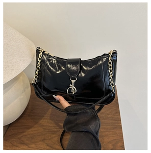 Detail of glossy black crescent shoulder bag with metallic spring buckle and gold chain strap