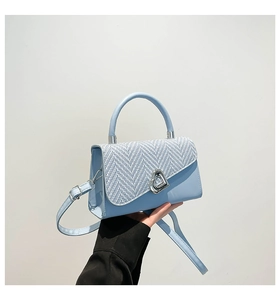 Detail of light blue crossbody bag with tweed flap and heart-shaped silver metal clasp