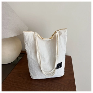 Detail of white canvas tote bag featuring black woven label on natural wood surface