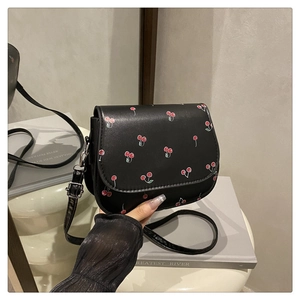 Close-up of black PU leather crossbody bag with vibrant red cherry print and silver buckle