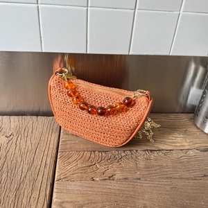Detail of orange woven half-moon bag with amber bead handle and gold chain strap