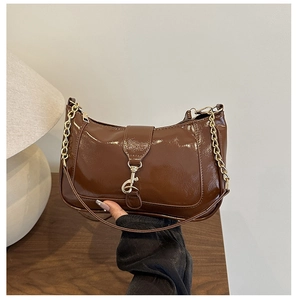Detail of dark brown glossy crescent bag with gold buckle closure and chain accent