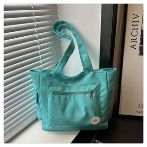 Detail shot of a mint green canvas tote bag with a front zipper pocket on a windowsill