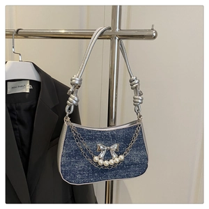 Close-up of blue denim shoulder bag with silver bow accent and pearl chain detail
