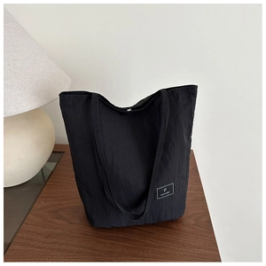 Detail of minimalist black tote bag with FANYISSA brand label on textured fabric