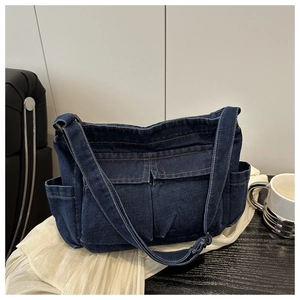 Macro shot of dark blue denim crossbody bag featuring dual front flap pockets and adjustable strap