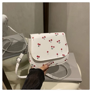 Detail showing white crossbody bag with cherry print and adjustable strap with silver buckle