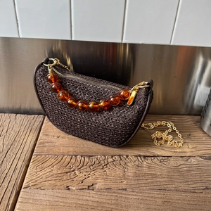 Detail of dark brown woven crescent bag with amber resin beads and gold chain strap