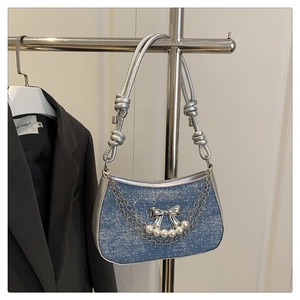 Detail of blue denim shoulder bag featuring silver metal bow and white pearl chain