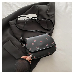 Close-up of small black PU leather crossbody bag with red cherry print on a suit background