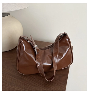 Detail of dark brown glossy hobo bag with adjustable strap and silver buckle on wood