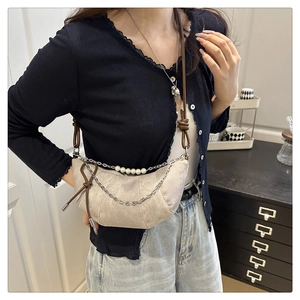 Chic beige crescent bag with pearl chain detail worn by model in a minimalist setting