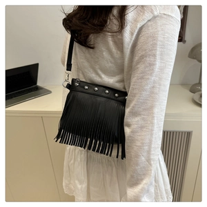 Borsa a secchiello nera alla moda con nappe e rivetti indossata da una modella in stanza