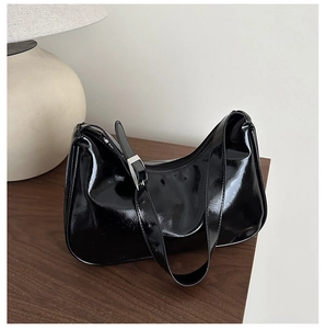 Close-up of black patent leather hobo bag with adjustable silver buckle strap on wooden table