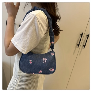 Denim underarm bag with floral embroidery and ruched shoulder strap worn by a model