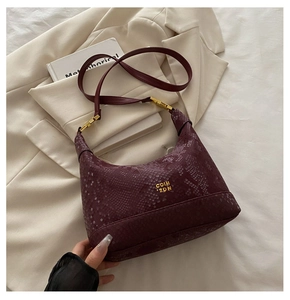 Close-up of burgundy hobo bag with snake pattern texture and gold logo detail