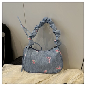 Close-up of light blue denim baguette bag with pink floral and bow prints and ruffled handle