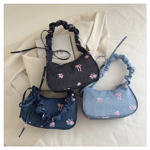 Detail of pink floral embroidery and bow accents on denim shoulder bag fabric