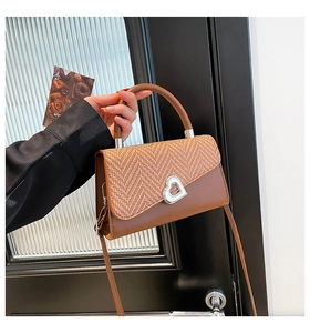 Detail of woven patchwork handbag with a silver heart buckle and brown leather strap