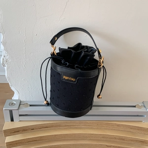 Détail du sac seau en cuir noir et textile avec inscription de marque dorée