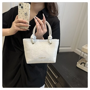 Detail of white snakeskin texture tote bag with braided handles and golden metal rings
