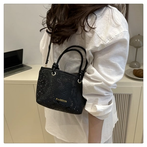 Detail of black snakeskin texture handbag with gold fashion lettering and round handle