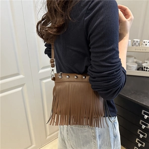 Brown tassel crossbody bag with silver studs and adjustable strap in a lifestyle setting