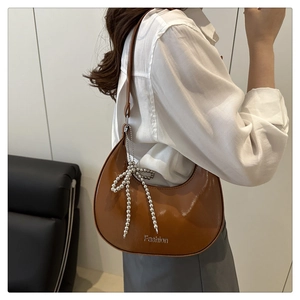 Détail d'un sac demi-lune marron avec une chaîne à billes argentée et nœud décoratif