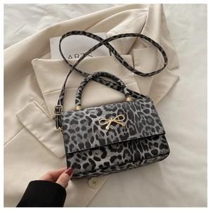 Détail d'un sac bandoulière léopard avec boucle nœud doré sur fond de veste de costume beige