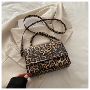 Détail du sac léopard avec fermoir nœud doré posé sur une veste de costume beige