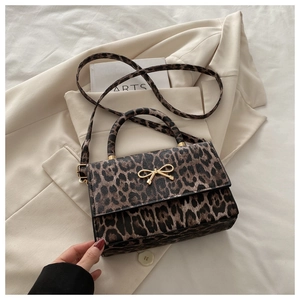 Détail d'un sac bandoulière léopard avec nœud doré sur un blazer élégant en fond