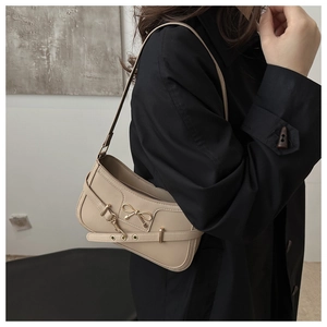 Sac bandoulière beige chic avec boucle nœud dorée porté sur un trench-coat noir élégant