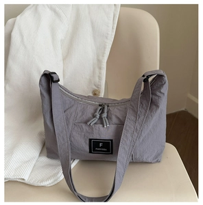 Macro detail of grey textured nylon tote bag featuring a brand logo on beige background