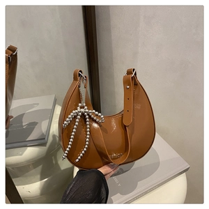 Détail d'un sac sous le bras demi-lune marron avec finition brillante et charm nœud argenté
