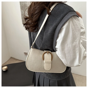 Detail einer cremefarbenen Vintage-Schultertasche mit Messingschnalle an einem Model-Outfit