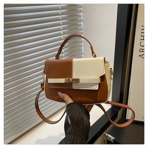 Detail of brown and white crossbody bag with gold turn-lock and visible stitching