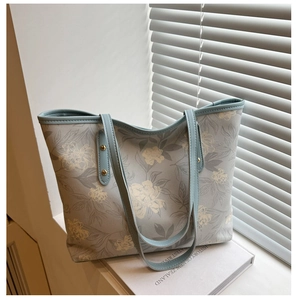Détail d'un sac cabas floral bleu clair avec anses fines et rivets dorés métallisés